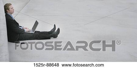 Business man in dark blue shirt and blue tie is sitting up against the concrete wall with his legs fully extended, typing on a laptop View Large Photo Image Stock Photo - Business man in dark blue shirt and blue tie is sitting up against the concrete wall with his legs fully extended, typing on a laptop. Fotosearch