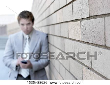 Business man is looking straight at you as he writes on his Pda against a tan brick wall View Large Photo Image Stock Photograph - Business man is looking straight at you as he writes on his Pda against a tan brick wall. Fotosearch