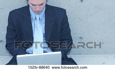 Business man with blue suit, blue shirt, and blue tie is sitting up against a concrete wall typing on his laptop View Large Photo Image Stock Image - Business man with blue suit, blue shirt, and blue tie is sitting up against a concrete wall typing on his laptop. Fotosearch