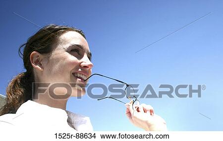 Business woman is wearing a white shirt and is biting her glasses. View Large Photo Image Picture - Business woman is wearing a white shirt and is biting her glasses.. Fotosearch