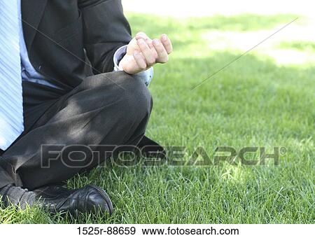 Stock Photo - Businessman in black suit, blue shirt, and blue tie is sitting meditation style in the green grass. Fotosearch