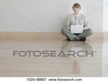 Stock Photo - Businessman in tan shirt and tie is typing on his white laptop on wooden floors. Fotosearch