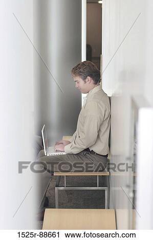 Businessman in tan suit is typing on his white laptop in the middle of an office building View Large Photo Image Stock Image - Businessman in tan suit is typing on his white laptop in the middle of an office building. Fotosearch