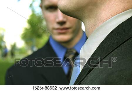 Stock Image - Businessman is stealthily looking at you from behind another businessman. Fotosearch