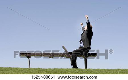 Businessman is waving his hands in celebration as he sits on a park bench, next to his laptop View Large Photo Image Stock Image - Businessman is waving his hands in celebration as he sits on a park bench, next to his laptop. Fotosearch