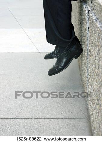 Businessman sits on the ledge with his feet inches from the ground View Large Photo Image Stock Image - Businessman sits on the ledge with his feet inches from the ground. Fotosearch