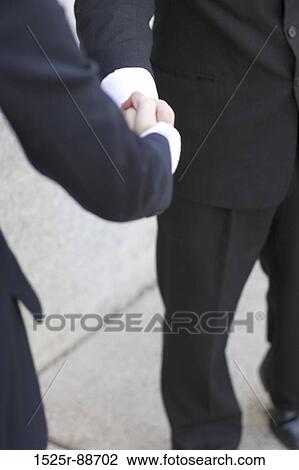 Stock Image - Businessman standing outside and gives another business woman a handshake. Fotosearch