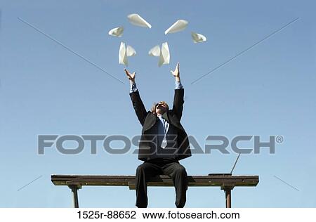 Businessman wearing black suit throws up all his papers in frustration as he sits on his park bench, next to his laptop View Large Photo Image Stock Image - Businessman wearing black suit throws up all his papers in frustration as he sits on his park bench, next to his laptop. Fotosearch