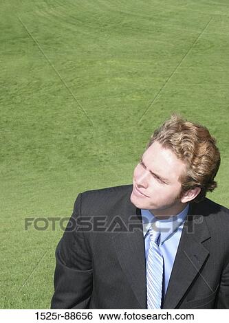 Businessman with black suit, blue shirt, and blue tie is looking up towards the sky in the green grass View Large Photo Image Stock Photograph - Businessman with black suit, blue shirt, and blue tie is looking up towards the sky in the green grass. Fotosearch