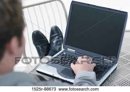 Businessman with gray shirt is putting his feet up on a chair as he types on his laptop with one hand. View Large Photo Image Stock Image - Businessman with gray shirt is putting his feet up on a chair as he types on his laptop with one hand.. Fotosearch