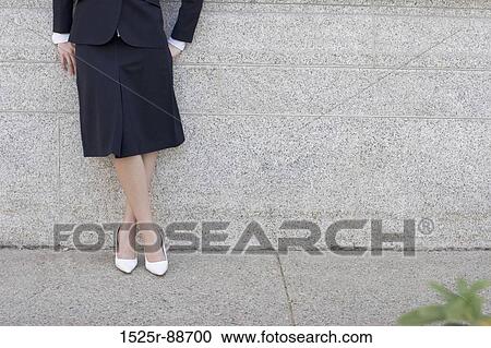 Businesswoman standing against the wall with her hands behind her back and her legs crossed View Large Photo Image Stock Image - Businesswoman standing against the wall with her hands behind her back and her legs crossed. Fotosearch