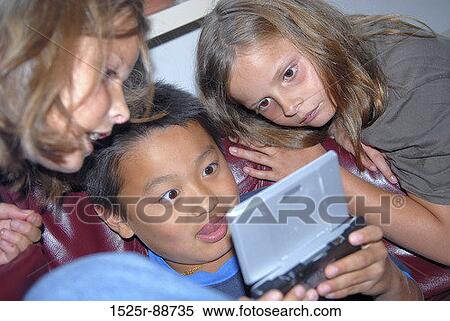 Boy playing a handheld video game with two girls leaning beside him View Large Photo Image Stock Photography - Boy playing a handheld video game with two girls leaning beside him. Fotosearch