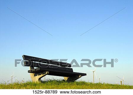 Stock Photo - Low angle view of a bench with wind turbines in the background. Fotosearch