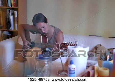 Mid adult woman sitting on a couch and playing a guitar View Large Photo Image Stock Photo - Mid adult woman sitting on a couch and playing a guitar. Fotosearch