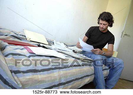 Young man sitting on the bed and reading a document View Large Photo Image Stock Image - Young man sitting on the bed and reading a document. Fotosearch