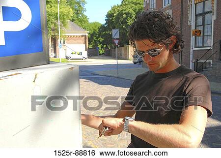 Young man standing near a parking sign and looking at his wristwatch View Large Photo Image Stock Photograph - Young man standing near a parking sign and looking at his wristwatch. Fotosearch