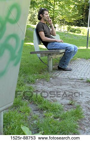 Young man talking on a mobile phone in a park View Large Photo Image Stock Image - Young man talking on a mobile phone in a park. Fotosearch