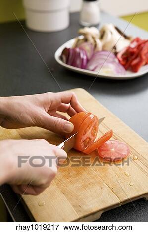 A detail image of a woman slicing tomatoes on a cutting board at home. - shallow depth of field with the focus on the tomato and knife View Large Photo Image Stock Photo - A detail image of a woman slicing tomatoes on a cutting board at home. - shallow depth of field with the focus on the tomato and knife. Fotosearch