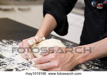 Stock Image - A young woman makes bread on the counter at home in the kitchen.. Fotosearch