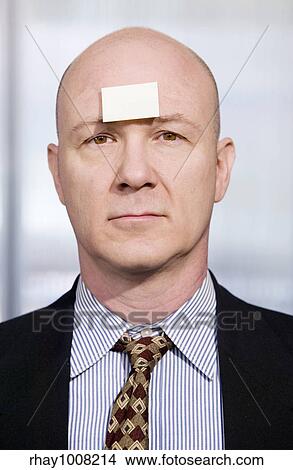 Picture - Bald businessman in with a blank sticky note on his forehead. Fotosearch