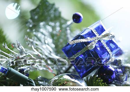 Stock Image - Blue present ornament nestled in CHristmas tree.. Fotosearch