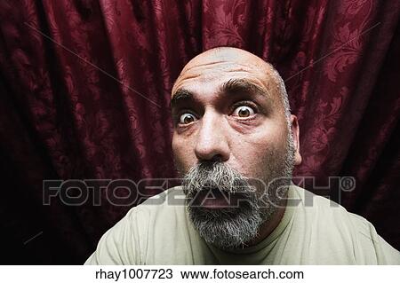 Stock Image - Close-up of a worried man in front of red curtains. Fotosearch