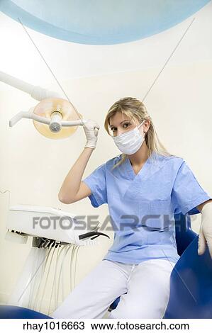 Stock Image - dental assistant smiling and adjusting the lamp. Fotosearch