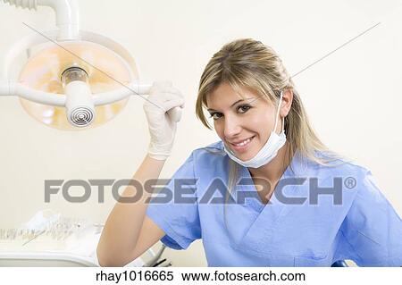 Stock Photography - dental assistant smiling and adjusting the lamp. Fotosearch