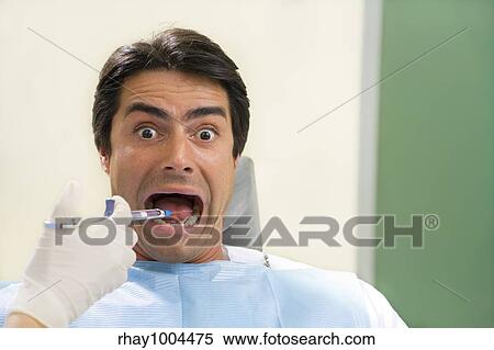 Stock Photography - dentist holding a syringe and anesthetizing his patient. Copy space on the right. Fotosearch