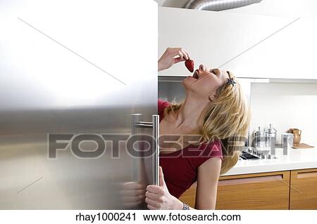Stock Image - domestic life: woman enjoying a juicy strawberry. Copy space on the left. Fotosearch