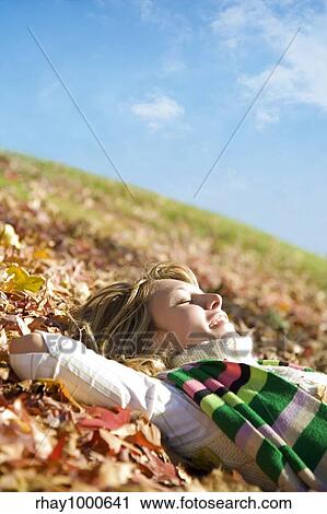 Stock Image - expressing positivity: blond girl resting on autumn leaves. Fotosearch