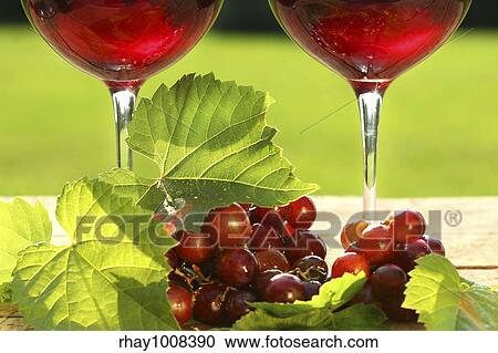 Stock Image - Glasses of red wine with grapes on a table. Fotosearch