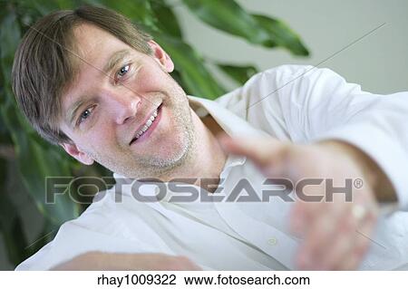 Stock Image - Handsome businessman in casual attire reaching out hand to give handshake.. Fotosearch