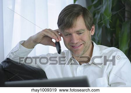 Handsome businessman working on laptop and using cell phone in casual attire. View Large Photo Image Stock Photo - Handsome businessman working on laptop and using cell phone in casual attire.. Fotosearch