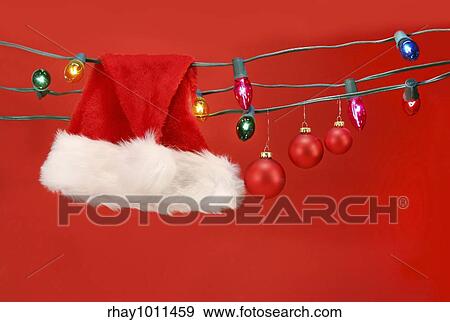 Hanging lights with santa hat and christmas balls against a red background View Large Photo Image Stock Photo - Hanging lights with santa hat and christmas balls against a red background. Fotosearch