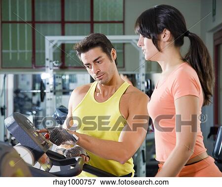 Stock Photo - health club: woman walking on a tapis roulant with her personal trainer. Fotosearch