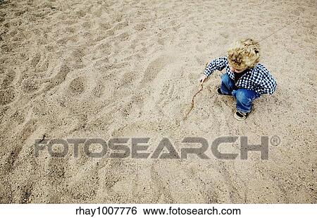 Little boy with a stick plays in a large patch of rough sand. View Large Photo Image Stock Photograph - Little boy with a stick plays in a large patch of rough sand.. Fotosearch
