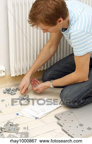 Stock Photo - "Man assembling a wardrobe. Parts, box and screwdriver on a white wooden floor. ". Fotosearch