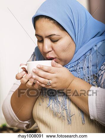 Muslim woman wearing a head scarf drinking coffee View Large Photo Image Stock Image - Muslim woman wearing a head scarf drinking coffee. Fotosearch