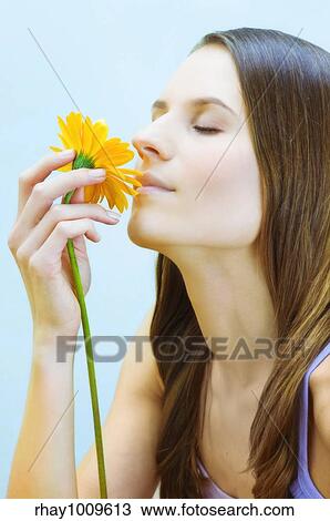 Stock Image - portrait of a girl smelling a flower that she holds in her hand. Fotosearch