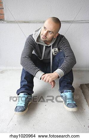 Portrait of a young man in his late twenties. Grey concrete background. Sitting bent forward with hands crossed. Contemplating young man. View Large Photo Image Picture - Portrait of a young man in his late twenties. Grey concrete background. Sitting bent forward with hands crossed. Contemplating young man.. Fotosearch