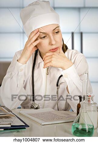"Portrait of the tired woman-therapist in a white uniform with a stethoscope, sitting near a table with records and medicinesPortrait of the tired woman-therapist in a white uniform with a stethos... " View Large Photo Image Stock Photo - "Portrait of the tired woman-therapist in a white uniform with a stethoscope, sitting near a table with records and medicinesPortrait of the tired woman-therapist in a white uniform with a stethos... ". Fotosearch
