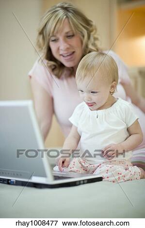 Stock Photo - Pregnant woman teaching baby daughter to use laptop. Fotosearch