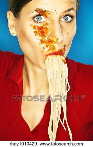 Stock Photo - pretty girl with tomato sauce all over her face sucking noodles. Fotosearch