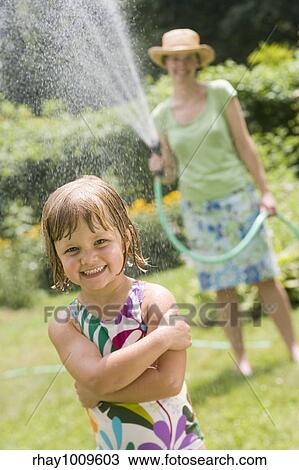 Pretty woman spraying little girl with water from a garden hose in the Summertime View Large Photo Image Stock Image - Pretty woman spraying little girl with water from a garden hose in the Summertime. Fotosearch