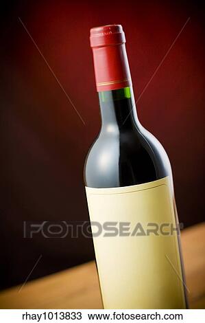 Stock Image - Red wine bottle on wooden table over dark red background. Fotosearch