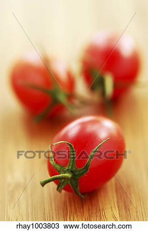 Stock Image - Small grape or cherry tomatoes on wooden cutting board. Fotosearch