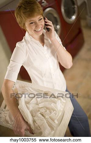 Smiling woman on cell phone holding laundry basket in laundry room View Large Photo Image Stock Photography - Smiling woman on cell phone holding laundry basket in laundry room. Fotosearch