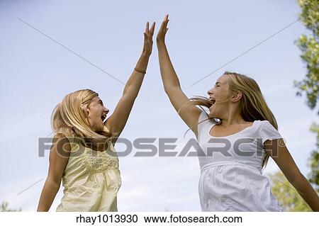 Stock Image - Teen girls celebrate winning by jumping in air and doing a high-five. Fotosearch