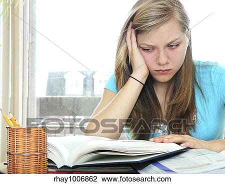 Stock Image - Teenage girl studying with textbooks looking unhappy. Fotosearch